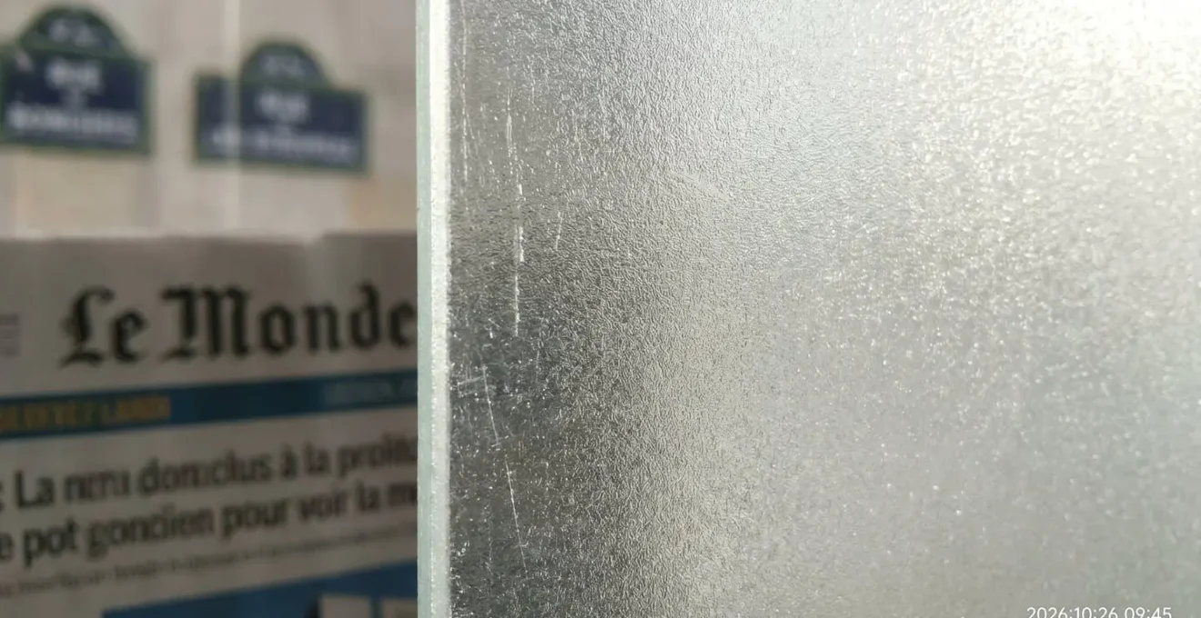 Gros plan sur la texture mate d'un panneau de verre dépoli traité à l'acide montrant la diffusion subtile de la lumière